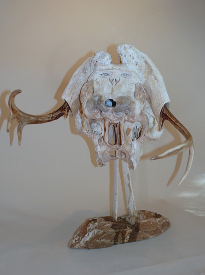 Manasie Akpaliapik, Janus-faced shaman
23 1/2 x 22 x 11 in.
SOLD
This is a tour de force that showcases Manasie's exceptional imagination and skill.  He has started with a caribou skull, and turned it upside down and backwards.  That is, the "front" of the sculpture is looking at the skull from behind and below the face.  There are two wonderful faces on the piece -- one on the front and one on the back.  The antlers have been moved and turned into arms.  In addition. to the faces, there is extensive carving on almost every surface of the piece.  The legs are made of ribs, and the assemblage stands on a stone base.  "One of a kind" does not begin to describe the originality of this piece.
03552-1