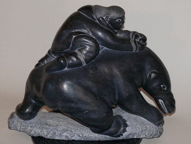 Lucassie Echalook, Hunter attacking bear with knife, c. 1970
15 x 17 x 8 in.
This dramatic, dynamic carving shows a hunter clinging to the back of a bear, with his knife embedded in the bear's back.  
Lucassie Echalook was raised on the land, and this carving vividly conveys the intensity of the hunter's struggle with the bear.  It is unusual in Lucassie's oeuvre for its extensive negative space.  It is also distinctive among many Inukjuak carvings for being fully realized in the round.  It does not have an obvious "front" and "back" -- as you rotate it, the composition has interest when viewed from any angle.
03705-1